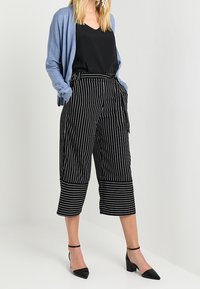 Schwarz-weiße gestreifte Culottes mit weitem Bein, hoher Taille und einem Bindegürtel. Kombiniert mit einem schwarzen V-Ausschnitt-Oberteil und einem hellblauen Cardigan.