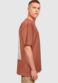 Brun kortærmet T-shirt med en afslappet pasform, der har et puslespilsdesign på ryggen og en ribbet rund halsudskæring.