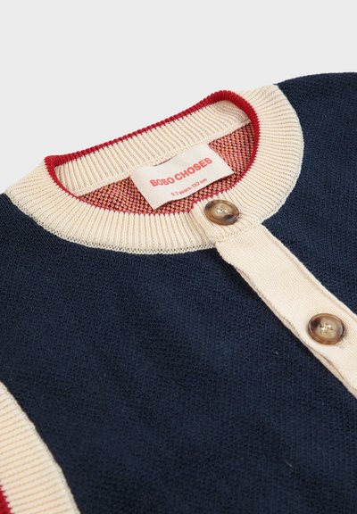 Cárdigan de punto azul marino con acentos crema, cuello redondo, dos botones y una etiqueta interior a rayas rojas. Adecuado para niños de 7 años (122 cm).