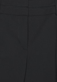 Primer plano de un pantalón de tela negra que muestra la pretina, las trabillas y el detalle de las costuras del bolsillo delantero.