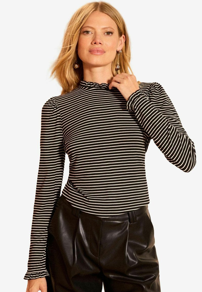 Fekete-fehér csíkos, hosszú ujjas topp, fodros gallérral és szűk ujjal, fekete, magas derekú bőrnadrággal párosítva.