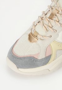 Sapatilha com materiais em malha e camurça nas cores beije, rosa, cinza e amarelo. Apresenta detalhes almofadados e atacadores decorativos entrelaçados.