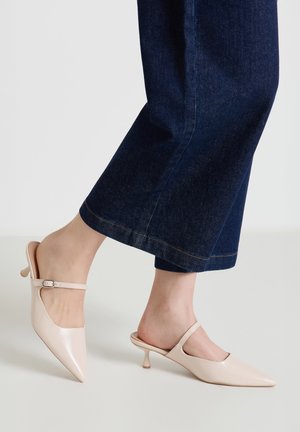 Hellrosa Slingback-Pumps mit spitzen Zehen und kleinem Absatz. Glattes, glänzendes Lackleder mit schmalem Knöchelriemen. Sichtbare Denim-Hose.
