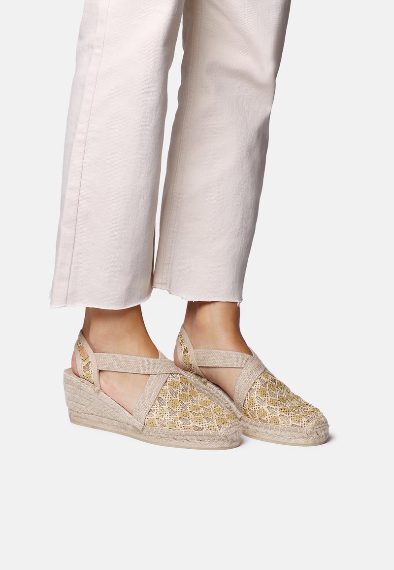 Espadrilles de cuña en color beige con un patrón tejido dorado, con tiras entrecruzadas y una suela de yute texturizada. Adecuadas para uso casual.