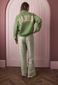 Green sweatshirt with "PARIS" printed in beige, paired with flared green checkered pants. Smooth texture and relaxed fit.