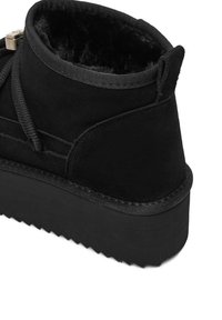 Botine negre din suede, cu un interior texturat, talpă groasă din cauciuc negru și formă rotunjită. Prezintă șireturi și o bucată de prindere la spate.