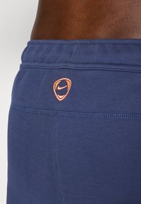 Navy blue shorts featuring a textured fabric and elastic waistband, with an orange Nike logo stitched near the back.