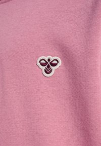 Rosa tyg med en texturerad yta, med en vit och mörklila broderad bi-emblem på vänster sida.