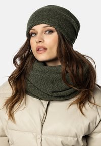 Cappello slouchy verde in maglia e sciarpa coordinata, entrambi realizzati in materiale testurizzato. Il cappello è morbido, mentre la sciarpa è spessa e avvolta.