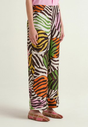 Femme portant un pantalon à jambes larges avec des cercles imprimés zèbre multicolores en orange, vert, jaune et rose, assorti à des ballerines pointues à motifs.