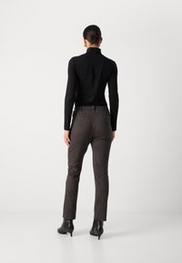 Haut noir à manches longues associé à un pantalon ajusté noir et blanc à pois, vu de dos, complété par des bottines à talons aiguilles noires.