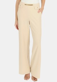 Beżowe spodnie o szerokich nogawkach wykonane z lekkiego materiału; posiadają złotą łańcuszkową ozdobę w pasie oraz dwie boczne kieszenie.
