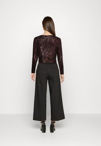 Schwarze, weit geschnittene Hosen kombiniert mit einem taillierten, mit Pailletten besetzten, dunkelvioletten Crop-Top. Das Outfit hat lange Ärmel und eine elegante Silhouette.