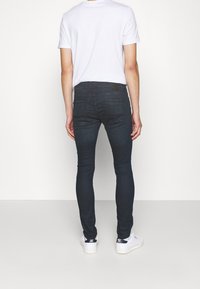 Tmavě modré skinny džíny s hladkou texturou a minimem švů, nošené s obyčejným bílým tričkem a bílými teniskami.