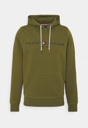 Olive green hoodie with front pocket, white drawstrings, and "Tommy Hilfiger Est. 1985" logo across the chest with a small flag emblem.