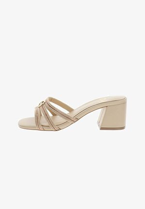 Sandale beige à talon ouvert avec trois brides tressées et talon bloc, ornée d'un petit ornement métallique circulaire.
