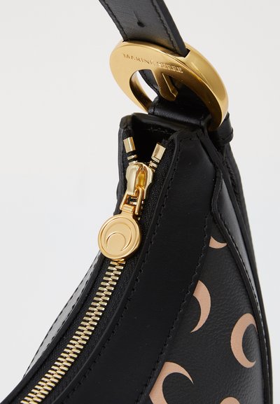 Bolso de cuero negro con herrajes dorados, que cuenta con un cierre y acentos circulares. El diseño incluye un patrón de lunas de color claro.