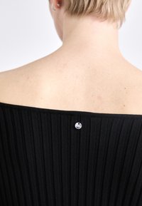 Black ribbed off-the-shoulder top with a smooth texture. Features a metallic button accent at the back near the neckline.