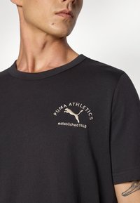 Sort bomulds T-shirt med korte ærmer, rund hals og et logo på brystet med en springende kat og teksten "PUMA ATHLETICS etableret 1948."