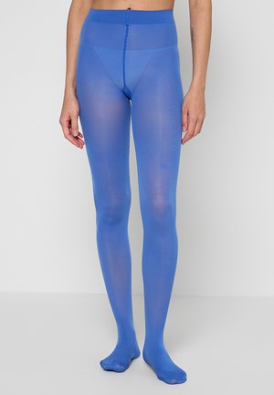 Person wearing sheer bright blue tights standing against a plain light gray background, showing legs and lower torso.