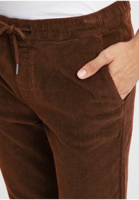 Brown corduroy pants featuring an elastic waistband with a drawstring, side pockets, and a soft, textured fabric.