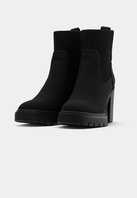 Crne gležnjače s teksturiranim rebrastim gornjim dijelom, debelim platformom i masivnom petom. Elegantan dizajn s glatkom završnom obradom.