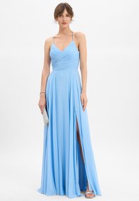 Hellblaues Abendkleid mit V-Ausschnitt, gefaltetem Oberteil, verstellbaren Spaghetti-Trägern und einem Schlitz bis zum Oberschenkel. Mit einer silbernen Clutch accessoriert.