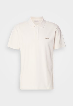 Kortermet, lys kremfarget polo skjorte i en glatt bomullsblanding. Har krage, tre knappestolper og et brodert logo på brystet.