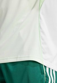Maglietta sportiva verde chiaro con una texture in rete traspirante, caratterizzata dal marchio AEROREADY e abbinata a pantaloni corti verde scuro con strisce bianche.