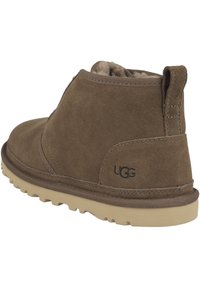 Stivale alla caviglia in suede marrone con superficie texturizzata, suola in gomma beige a contrasto e logo UGG sul lato. Caratterizzato da un profilo basso e punta arrotondata.