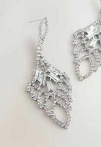 Pendientes de plata con un intrincado diseño en forma de hoja, que presentan rhinestones claros y acentos rectangulares, mostrando un acabado texturizado y brillante.