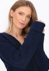 Maglione lavorato a maglia di un blu navy con scollatura a V profonda, polsini a costine e una consistenza morbida, caratterizzato da una vestibilità comoda e dettagli di cucitura in vista.