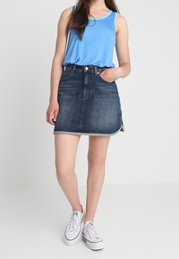 Denim A-linje kjol i mörkblått med en diskret frans vid fållen, ihopparad med en ljusblå tank top och vita sneakers.