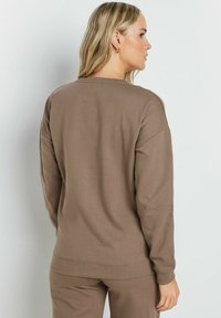 Felpa in cotone marrone con collo rotondo, polsini e orlo a coste. Texture morbida e vestibilità rilassata, dettagli di cucitura visibili.