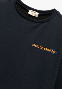 Granatowy bawełniany sweatshirt z okrągłym dekoltem, z pomarańczowym napisem "SPEED UP, GAME ON" z niebieskimi akcentami, gładką teksturą i swobodnym stylem.