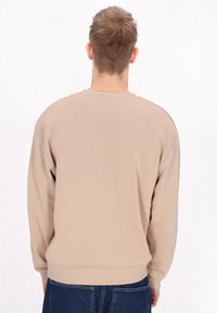 Beige színű pulóver, kerek nyakkivágással és esett vállakkal. Hosszú ujjakkal, bordás mandzsettákkal és aljjal rendelkezik, puha, texturált anyagból készült.