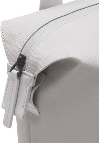 Sac à dos en tissu texturé gris avec fermeture éclair, présentant un tirette de fermeture éclair blanche et des détails de couture distincts le long des bords.