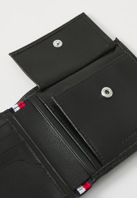 Portefeuille en cuir noir avec fermeture à pression, comportant des emplacements pour cartes et un accent intérieur aux rayures rouges, blanches et bleues. Texture lisse et design durable.