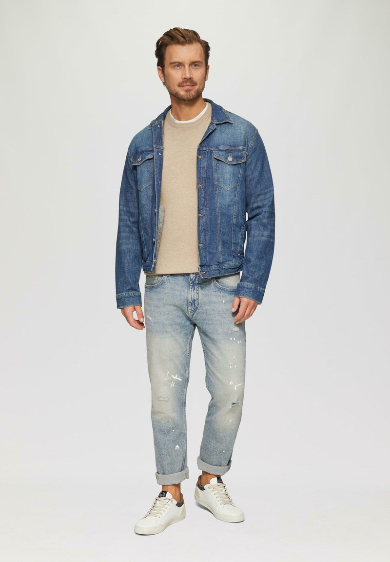 Zila džinsā jaka, gaiši pelēks džemperis, izbalējuši gaiši zili džinsi ar nolietotiem elementiem un balti sporta apavi ar pelēkiem akcentiem.