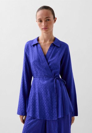 Top avvolgente in un vibrante blu reale, con colletto, maniche lunghe e una cintura regolabile in vita; realizzato in un tessuto liscio e strutturato.