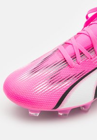 Scarpa da calcio rosa con tomaia testurizzata, caratterizzata da strisce diagonali nere e bianche e una suola traslucida. Design con lacci.