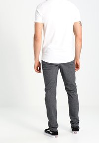 Grijze, gestructureerde broek met een slim fit, gecombineerd met een wit overhemd met korte mouwen en zwarte sneakers. De outfit is eenvoudig en casual.