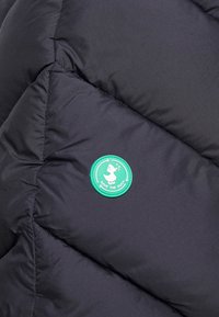Tejido de chaqueta acolchada negra con patrón de rombos acolchados. Presenta un parche redondo de tela verde con un logo de pato y el texto "SAVE THE DUCK".