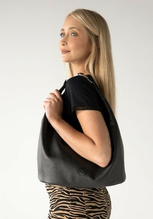 Borsa a spalla in pelle nera con una texture morbida, forma curva e dettagli in argento sulla tracolla. Indossata al braccio su uno sfondo neutro.
