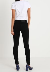Jeans ajustados negros de cintura media, con un diseño clásico de cinco bolsillos y un ligero estiramiento, combinados con una camiseta blanca simple y tacones azules.