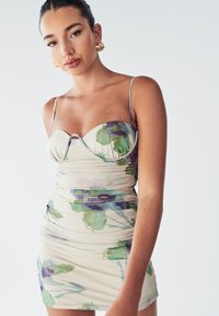 Bloemige bodycon jurk in crème met groene en paarse aquarel patronen, zachte stof, aansluitend ontwerp en dunne banden.
