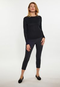 Zwarte langemouwen trui, gecombineerd met donkergrijze fitted broek. Zachte stof met een gladde textuur. Zwarte instappers met gouden accenten.