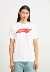 Balts kokvilnas T-krekls ar lielu sarkanu Formula 1 logo priekšā. Īsas piedurknes un apaļa kakla izgriezums. Ikdienišķa, brīva piegrieze.