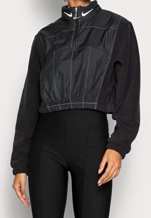 Veste noire courte zippée avec un col haut, fabriquée à partir d'un matériau lisse avec des coutures contrastées et un logo de la marque au niveau du col.
