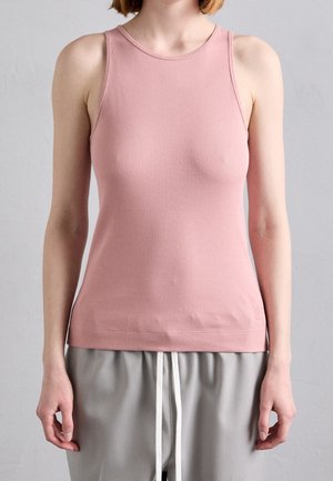 Kobieta w różowej prążkowanej koszulce bez rękawów i jasnoszarych spodniach na sznurku na jednolitym szarym tle.